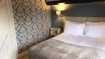 A hotel room with a bed, a nightstand, a wall-mounted lamp, and a patterned wallpaper.