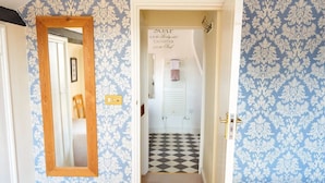 A hallway with patterned wallpaper, a checkered floor, a mirror, and a door leading to a bathroom. - Coachmakers Arms (Wallingford)