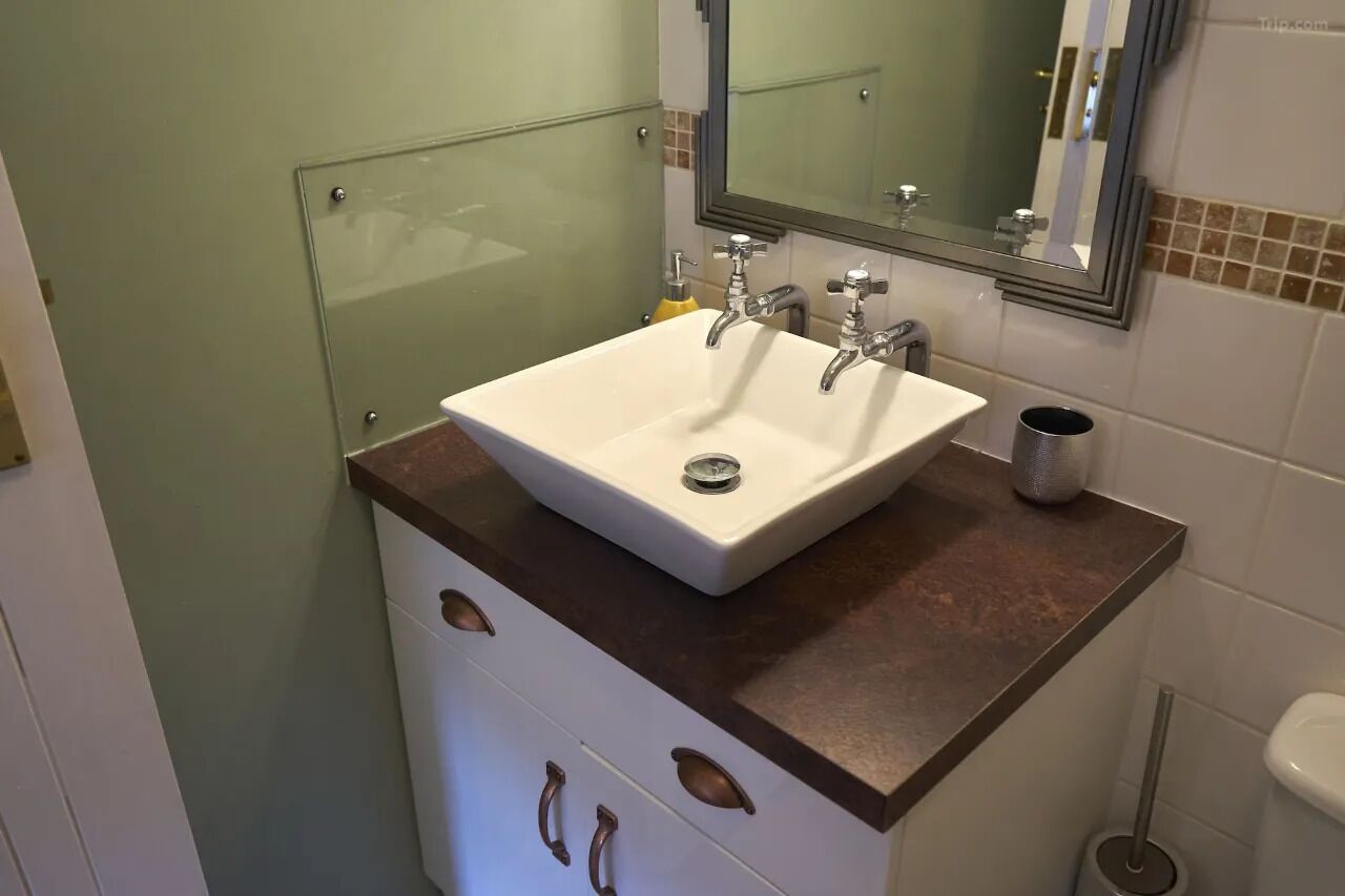 A bathroom with a white sink, two faucets, a mirror, and a toilet.