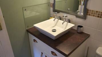 A bathroom with a white sink, two faucets, a mirror, and a toilet.