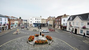 A town square with cobblestone pavement, a central statue, and surrounding buildings including a bank and shops. - Coachmakers Arms (Wallingford)