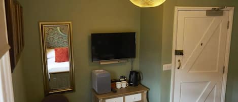 A room with a television, a small table with a coffee maker, a chair, and a door.