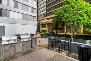 An outdoor patio with a barbecue grill, seating area, and a view of a modern building. - Modern Arlington - Only two Metro stops (Arlington)