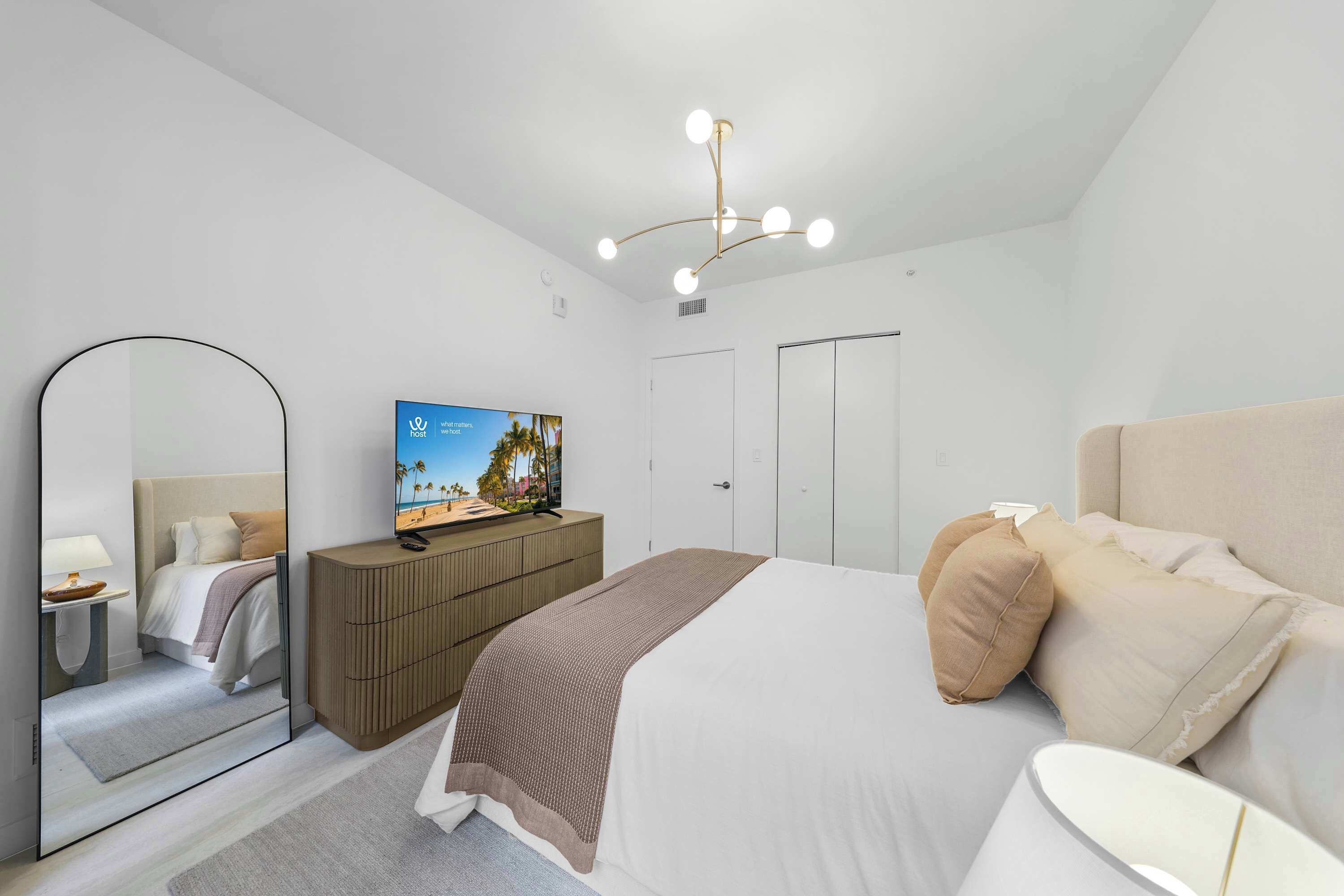 A modern hotel room with a bed, a television, a wardrobe, and a mirror.