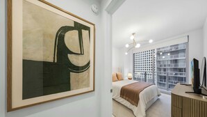 Una camera da letto moderna con un grande quadro astratto, un letto con coperta a righe beige e marrone, un comodino con lampada e una TV su un supporto in legno.