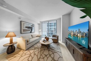 A modern living room with a sofa, armchair, coffee table, and a television displaying a cityscape. - Luxury 1-Bedroom Residence at Viceroy Brickell (Miami)