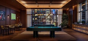 Ein Billardtisch in einem Raum mit Blick auf die Stadt, einer Bar und großen Fenstern.