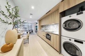 A modern kitchen with wooden cabinets, a built-in oven, a double-door washing machine, and a dining area with a table and chairs. - Luxury 1-Bedroom Residence at Viceroy Brickell (Miami)