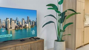 Un televisore mostra una veduta della città con il logo 'host', una pianta in vaso e mobili in legno.