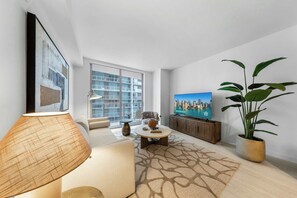 Ein modernes Wohnzimmer mit einer Couch, einem Couchtisch, einer Lampe, einem Fernseher und einem großen Fenster.