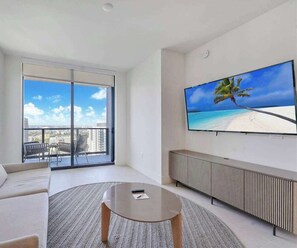 Un salon moderne doté d’un grand téléviseur, d’un canapé, d’une table basse et d’un balcon offrant une vue sur la ville.