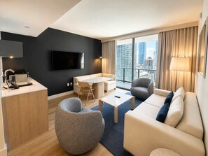 A modern hotel room with a flat-screen TV, a dining area, a sofa, and a view of the cityscape. - Chic 1BR Downtown Condo | Pool & Skyline Views (Miami)