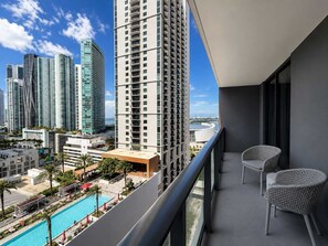 A balcony with two wicker chairs, overlooking a swimming pool and high-rise buildings. - Chic 1BR Downtown Condo | Pool & Skyline Views (Miami)
