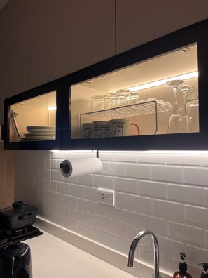 A kitchen with a built-in shelf holding mugs and glasses, a roll of paper towels, and a coffee maker. - Rincón del Atardecer Boutique Apartment (Arequipa)