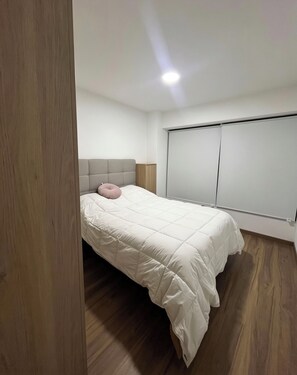 A bedroom with a bed, a headboard, a window with blinds, and a wooden floor. - Rincón del Atardecer Boutique Apartment (Arequipa)