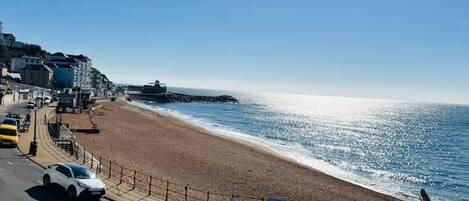 A coastal road with a beach on one side and buildings on the other.