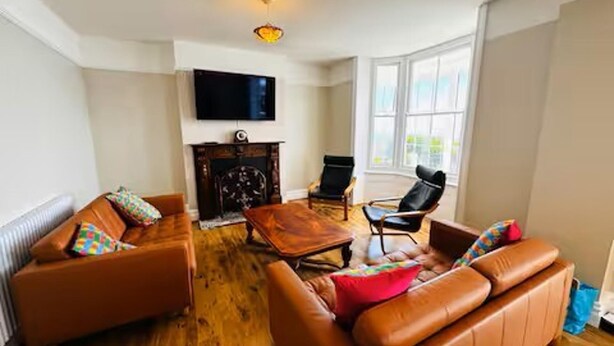 Una sala de estar con sofás de cuero, una mesa de centro de madera, chimenea y televisor montado en la pared.