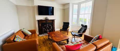 Un salon avec des canapés en cuir, une table basse en bois, une cheminée et un téléviseur fixé au mur.
