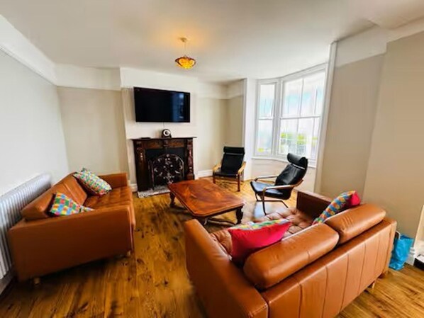A living room with leather sofas, a wooden coffee table, a fireplace, and a television mounted on the wall. - Ventnor 4-bed House, Sleeps 8, Parking & Pets Ok (Ventnor)