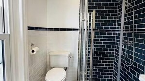 Et badeværelse med toilet, brusebad og flisebeklædt væg.