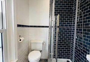 A bathroom with a toilet, a shower, and a tiled wall. - Ventnor 4-bed House, Sleeps 8, Parking & Pets Ok (Ventnor)
