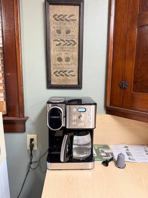 A coffee maker on a wooden counter with a framed sign above it.