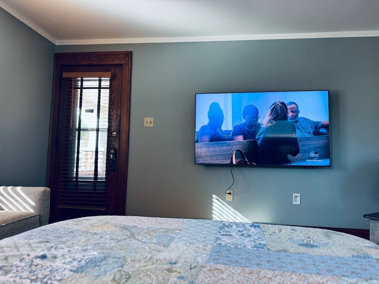 Un dormitorio con una cama, un televisor en la pared, una puerta y una ventana.