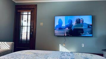Un dormitorio con una cama, un televisor en la pared, una puerta y una ventana.