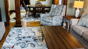 Un salon avec une table basse en bois, des canapés à motifs et un coin repas comprenant une table et des chaises en bois.