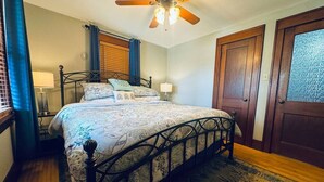 Une chambre à coucher avec un lit, un ventilateur de plafond, une fenêtre avec des rideaux et une porte.