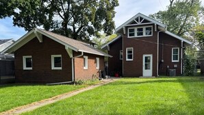 Une maison à deux étages, construite en briques, avec un jardin devant et un chemin menant à l’entrée.