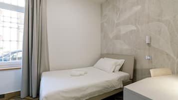 A single bed with a headboard, a bedside table, a wall-mounted light, and a window with curtains.