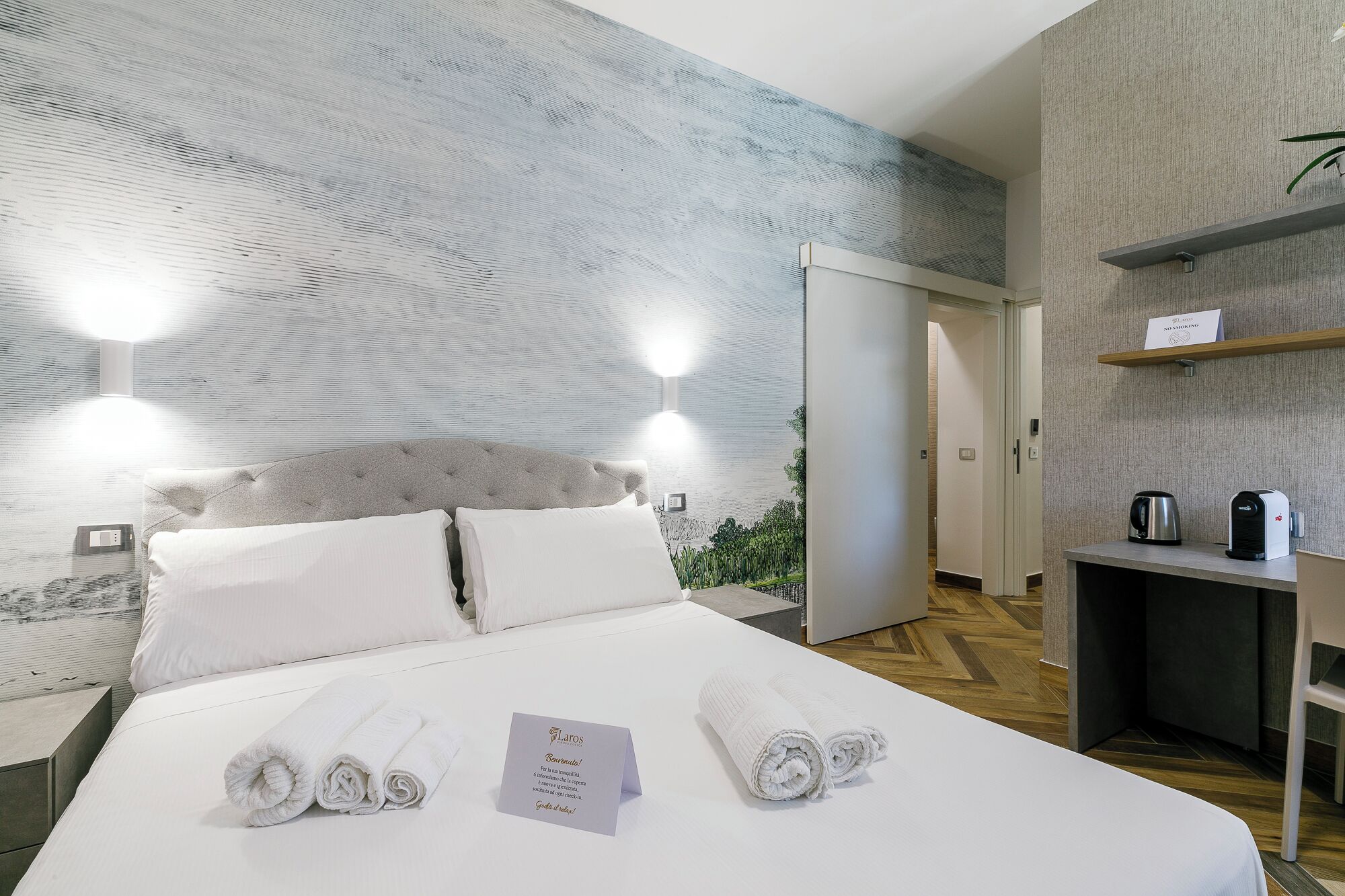 A hotel room with a large bed, two pillows, a note, and a towel.