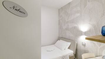 A hotel room with a bed, a wall-mounted light, a wooden shelf, and a sign with the name 'Nabucco'.