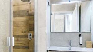 Un baño moderno con cabina de ducha de vidrio, tocador de madera y espejo sobre el lavabo.