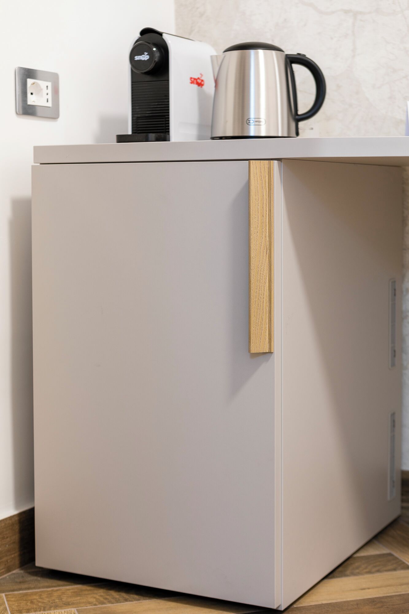Un refrigerador compacto y moderno con un tirador de madera, una cafetera y un hervidor encima.