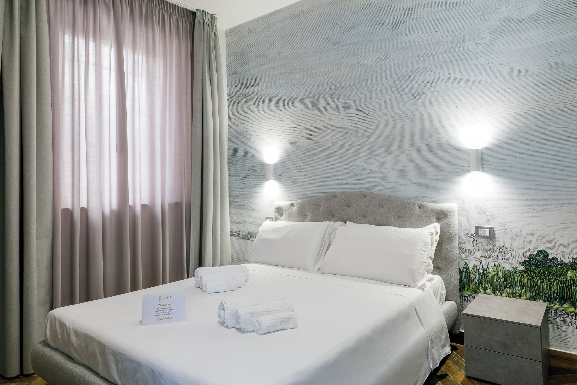 Una habitación de hotel con una cama bien tendida, una mesita de noche y una lámpara de pared.