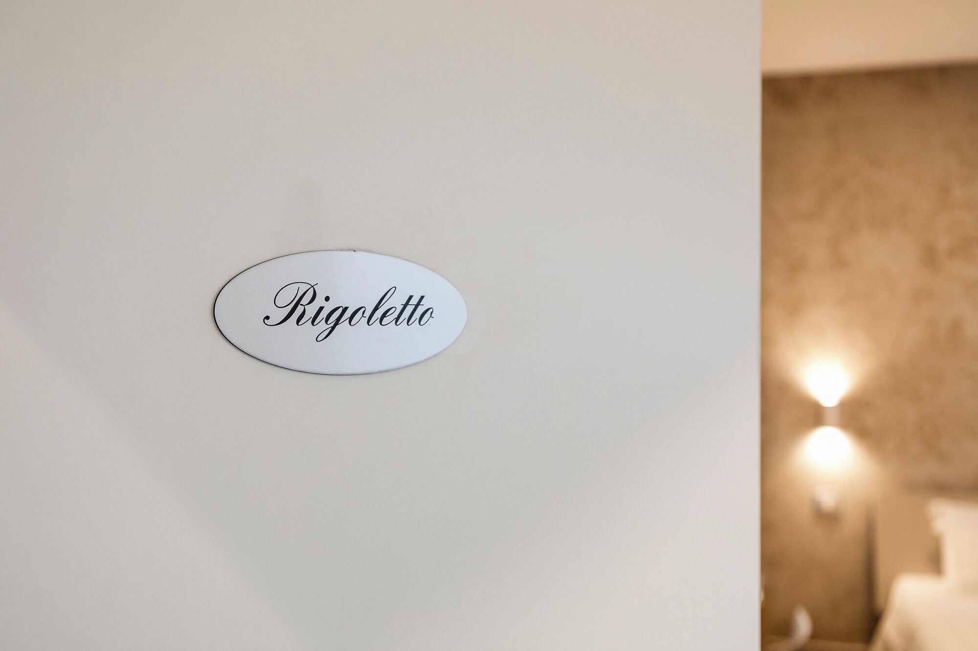 Un mur blanc sur lequel est apposé un panneau ovale portant l’inscription « Rigolettto ».