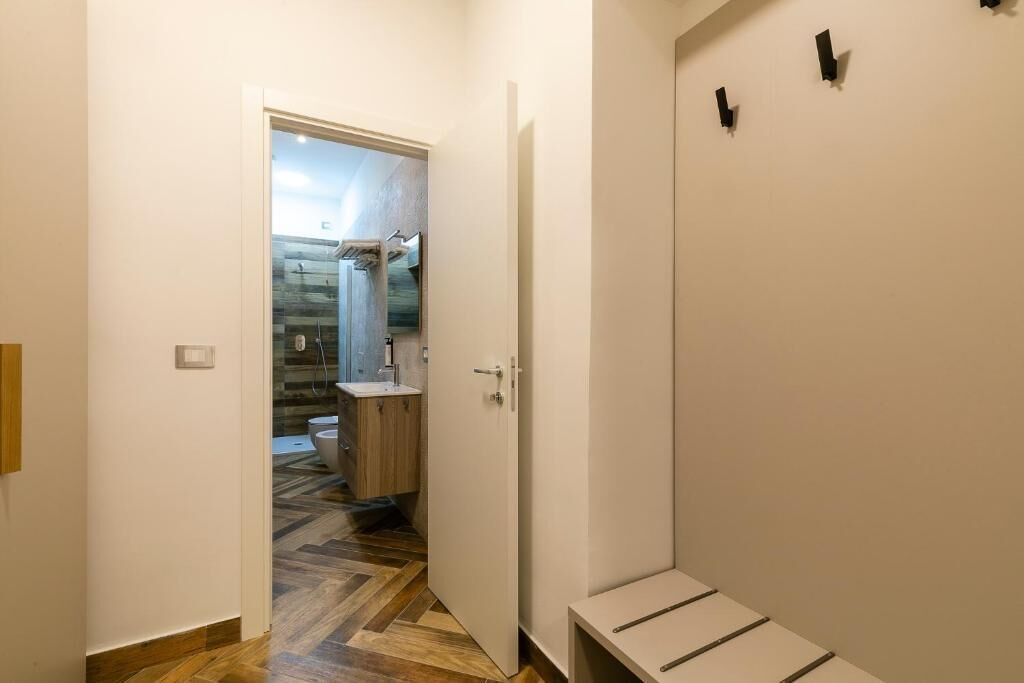 A hallway with a wooden floor leading to a bathroom with a shower and toilet.