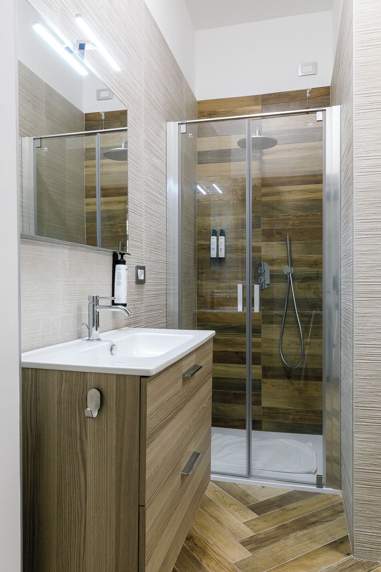 Un bagno moderno con doccia vetrata, mobile lavabo in legno e uno specchio grande.
