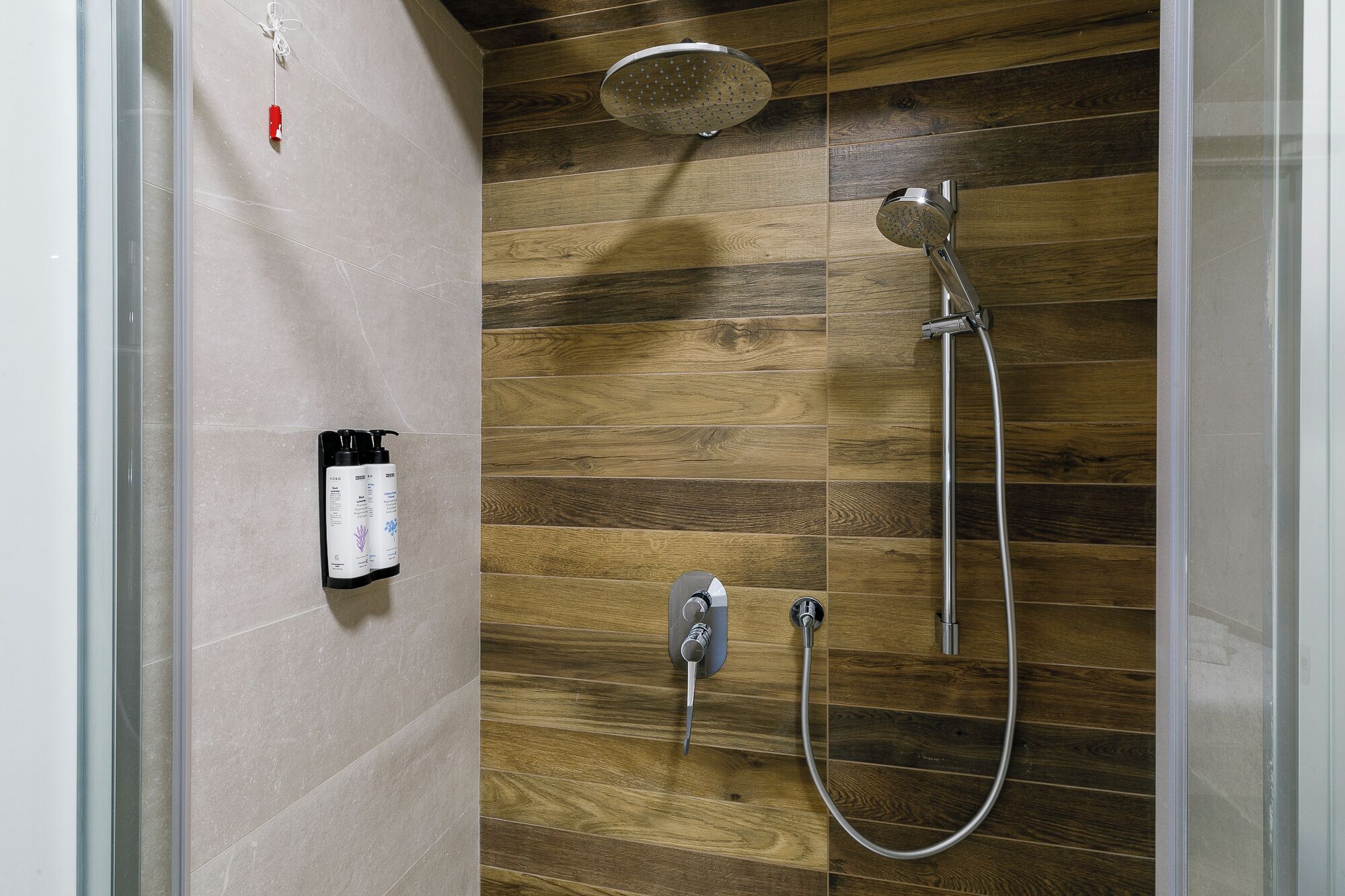Une douche avec un mur en panneaux de bois, un pommeau de douche à main et un robinet fixé au mur.