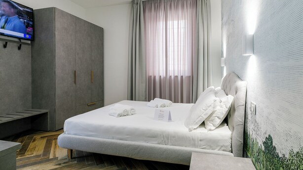 Una habitación de hotel con cama, televisión, armario y ventana con cortinas.