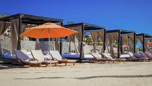 A beachside lounge area with sun loungers and umbrellas, stone walls, and a clear blue sky. - Pueblo Bonito Sunset Beach Suite with 2 bedrooms/AC in pleasant Cabo San Lucas (Cabo San Lucas)