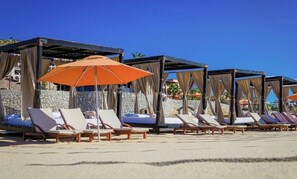 Eine Strandlounge mit Liegestühlen und Sonnenschirmen, Steinmauern und einem strahlend blauen Himmel.