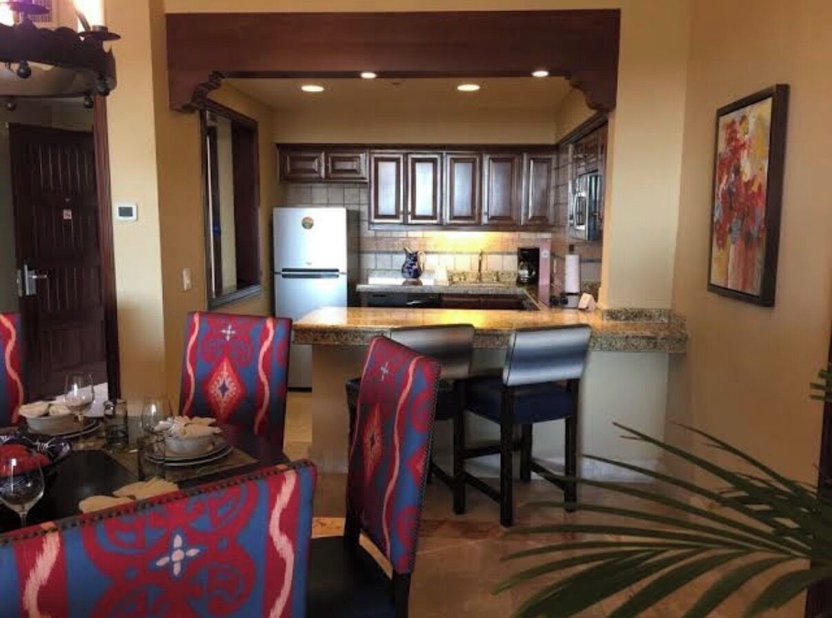 Una cocina con una isla central, armarios de madera oscura y un comedor con sillas estampadas.
