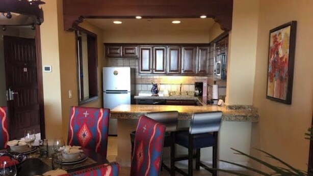 A kitchen with a central island, dark wooden cabinets, and a dining area with patterned chairs. - Pueblo Bonito Sunset Beach Suite with 2 bedrooms/AC in pleasant Cabo San Lucas (Cabo San Lucas)