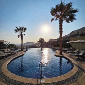 Ein kreisförmiger Infinity-Pool mit Liegestühlen und Palmen, umgeben von einer Poollandschaft mit freiem Blick auf die Landschaft.