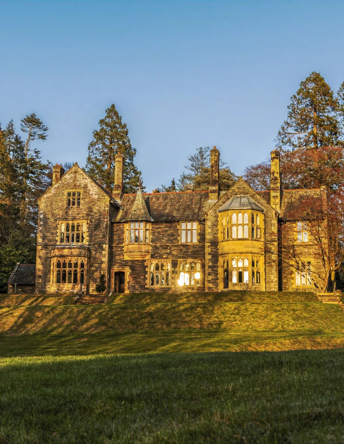 A large stone building with multiple chimneys, large windows, and a sloped roof.