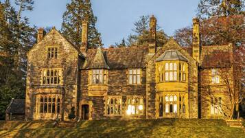 A large stone building with multiple chimneys, large windows, and a sloped roof.