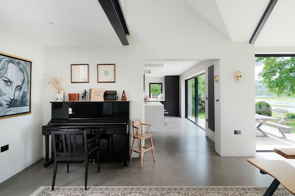 A modern interior with a piano, chairs, a desk, and a large window offering a view of the outdoors.